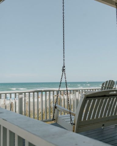 Covered oceanfront deck with hanging swing and Adirondack chairs overlooking beach and sea