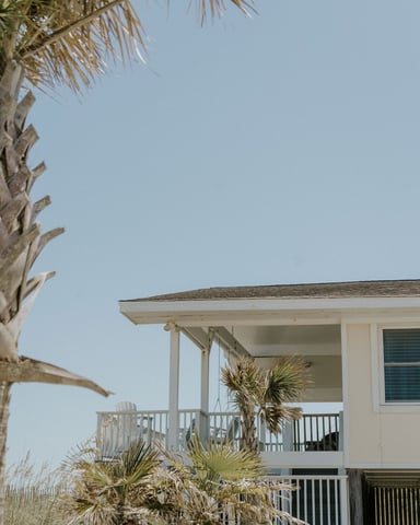 Beachfront house with white balcony and palm trees against a clear blue sky