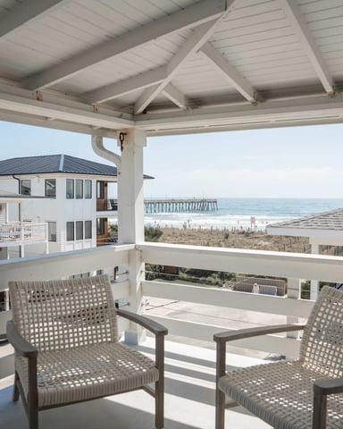Aerial view of beachfront homes with dunes, beach umbrellas, and ocean waves with swimmers