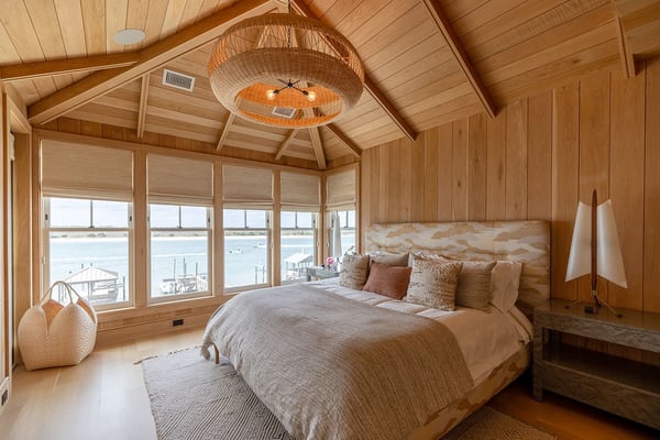 Wooden bedroom with vaulted ceiling, woven pendant light, and waterfront views through large windows