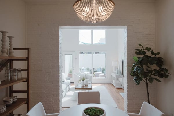 Bright open-plan living space with white brick walls, beaded ceiling fixture, and glass doors opening to a terrace with ocean view