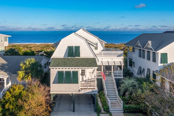 Elevated beachfront house with white exterior, green shutters, and wooden deck overlooking ocean and dunes.